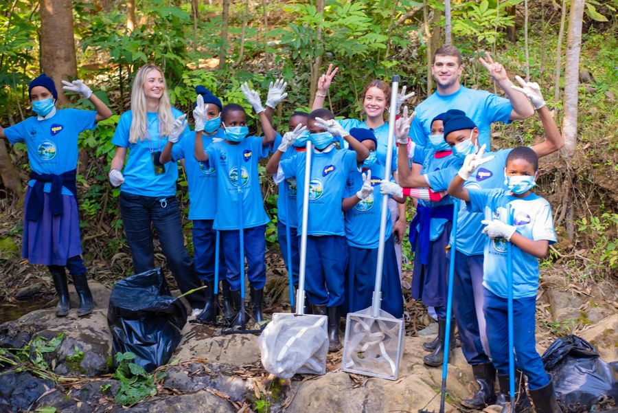 A large group of students and volunteers celebrating at the end of a KIWI river cleanup day