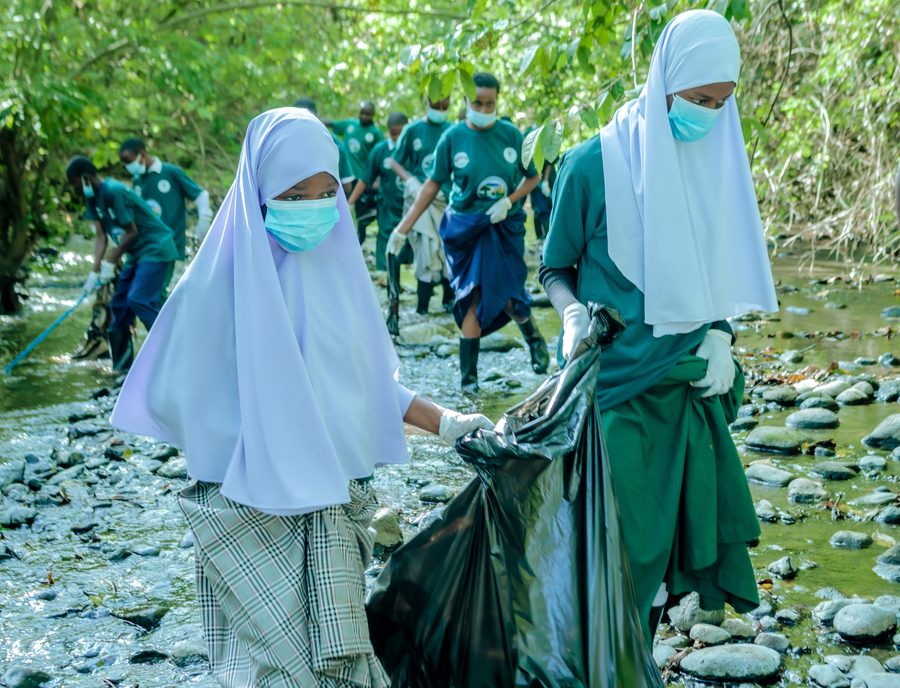 Two students carrying a full waste sack across the rocky riverbed
