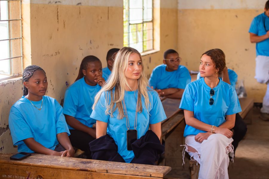 Visiting volunteers sitting among students on the classroom benches during a KIWI water education session