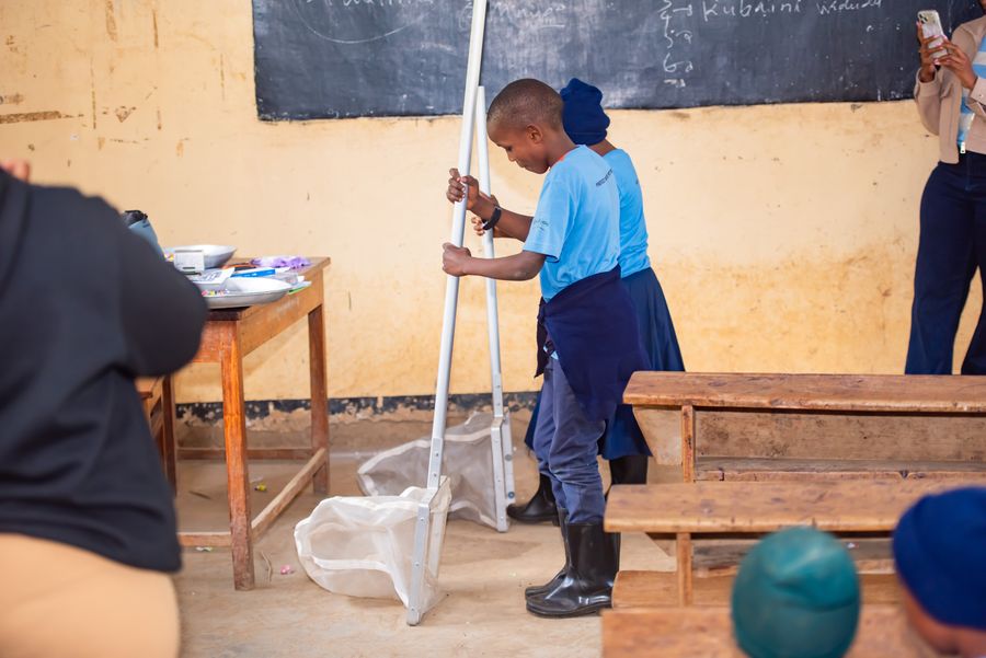 A student holding a river sampling net at the front of the classroom while equipment is set out on the desk